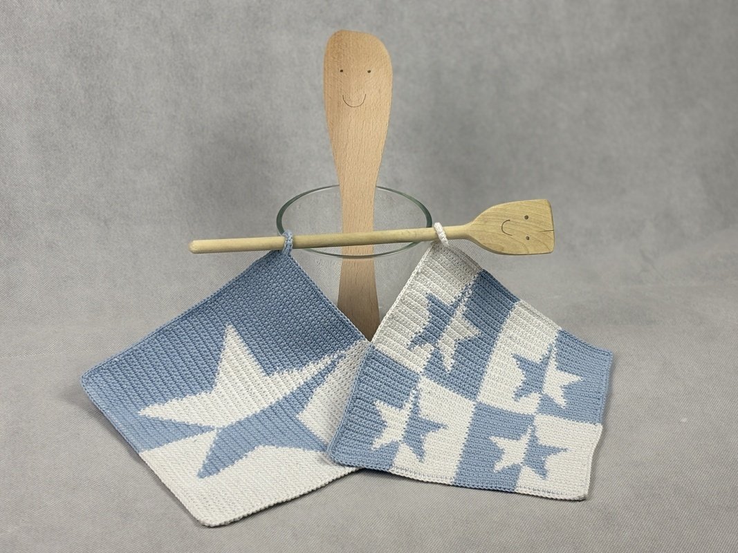 Pair of blue and white crocheted potholders with star motifs hanging from wooden utensils.
