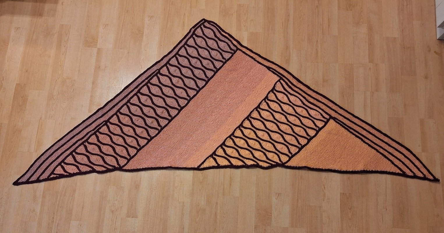 Gestricktes Dreieckstuch in Pfirsich- und Dunkelbrauntönen mit Wellen- und Blockmustern auf hellem Holzboden