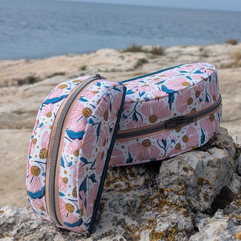 Zwei Kosmetiktaschen mit rosafarbenem Blumenmuster und Reißverschluss auf Felsen am Meer.