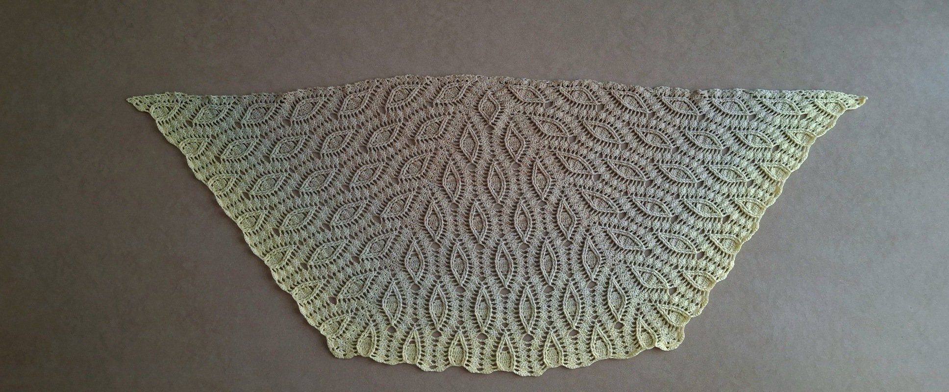 Flat-lay triangular cream crochet shawl with repeating leaf lace motifs and scalloped edge