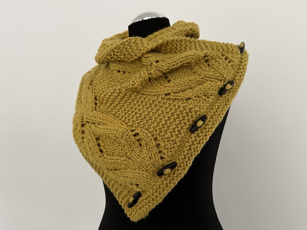 Senfgelber gestrickter Kragenschal mit seitlicher Knopfleiste und Zopfmuster auf schwarzer Schaufensterpuppe