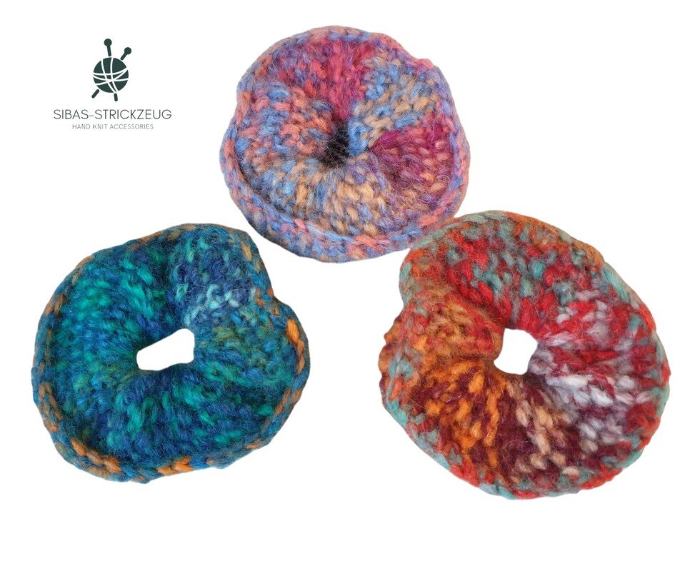 Drei bunte, gestrickte Haargummis in Blau-Grün, Pink-Lila und Rot-Orange auf weißem Hintergrund