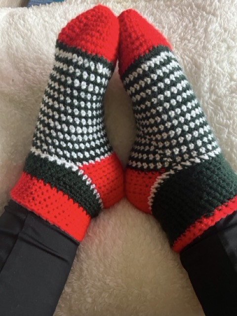 Gehäkelte rot‑dunkelgrüne Socken mit weißem Punktemuster, getragen