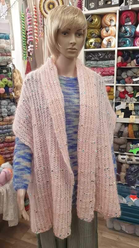 Schaufensterpuppe mit rosa, flauschigem Rechtecktuch mit Pailletten vor Regalen mit Wolle