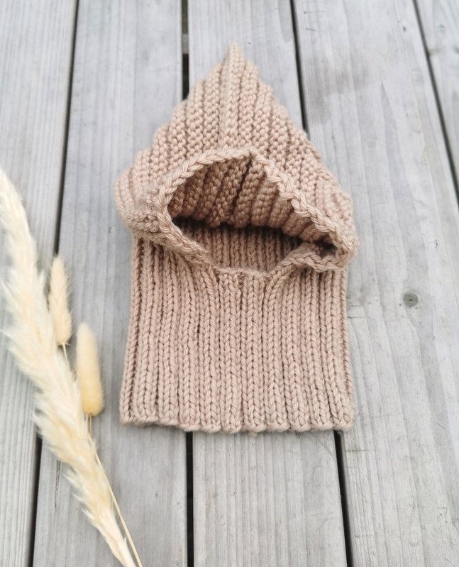 Beigefarbene, gerippte Strick-Sturmhaube für Baby oder Kind auf hellem Holzboden mit Pampasgras.