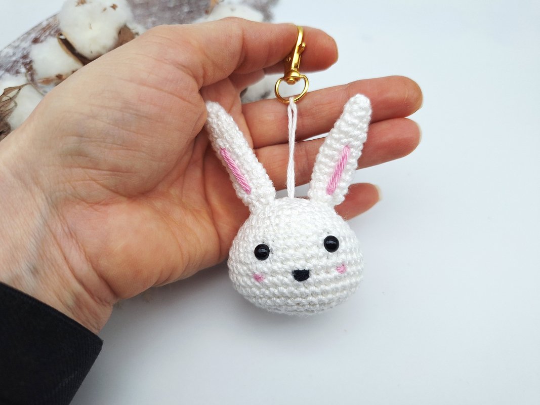 Gehäkelter weißer Hasen‑Schlüsselanhänger mit rosa Ohren und goldfarbenem Karabiner in einer Hand