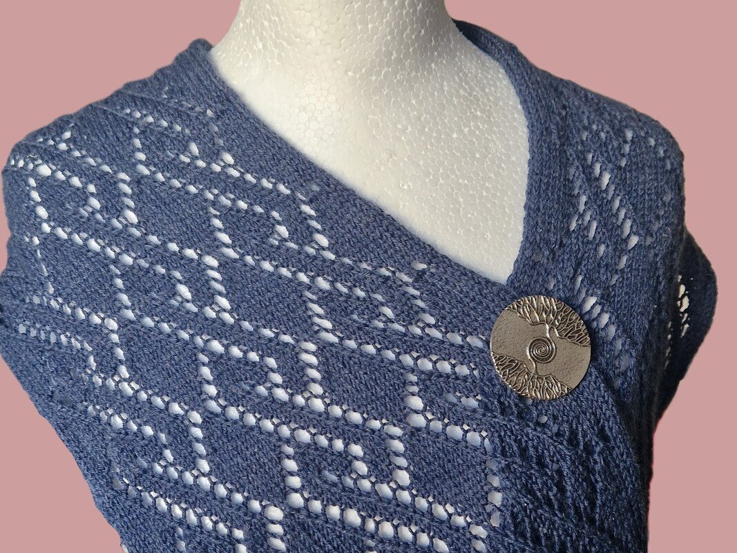 Blaues Lacetuch mit Rautenmuster und runder dekorativer Nadel an einer Büste