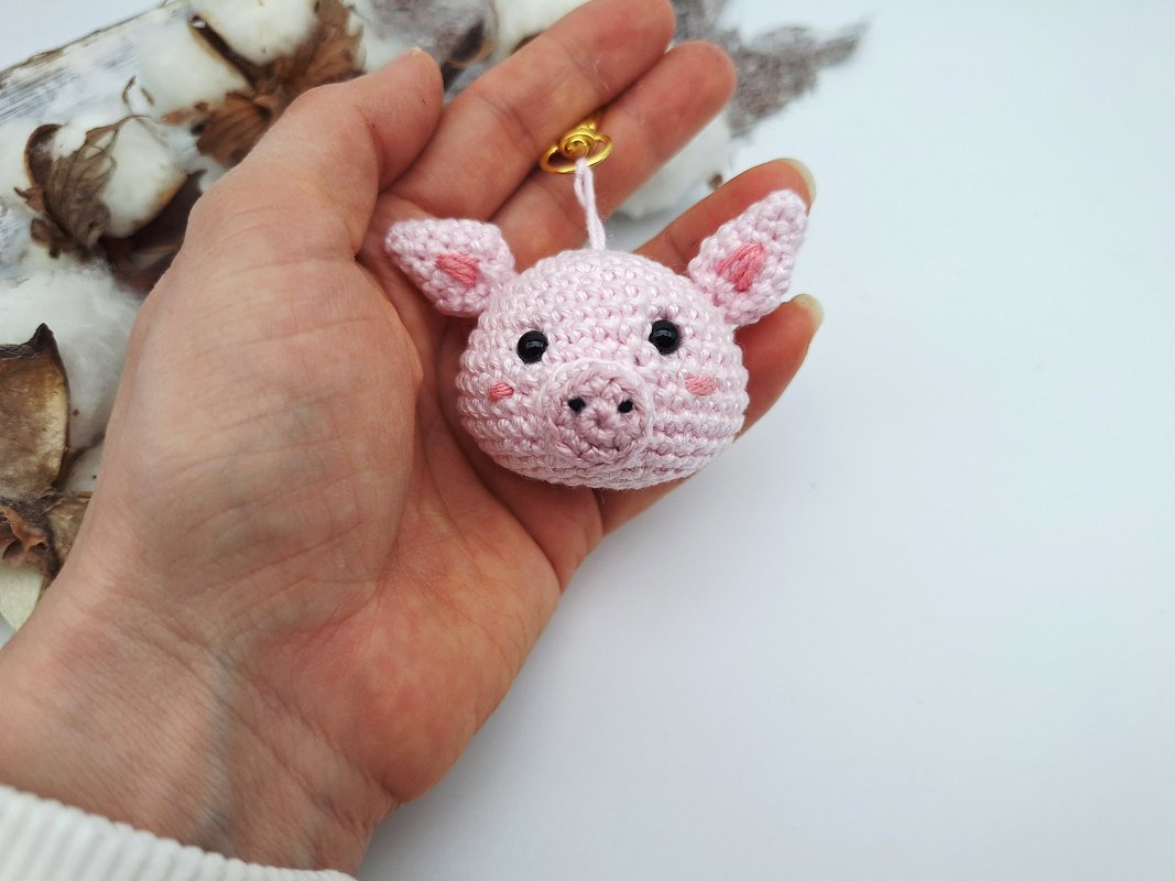 Gehäkeltes rosa Schweinchen mit Öse in Hand, Dekoration im Hintergrund