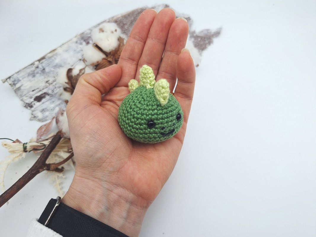 Hand hält kleinen grünen gehäkelten Dino mit hellgelben Stacheln