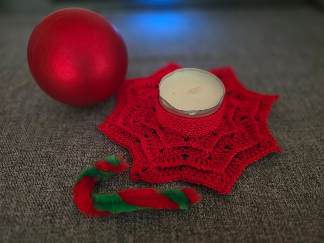 Roter Stern-Untersetzer gehäkelt mit eingesetztem Teelicht, daneben rote Kugel und grün-roter Zuckerstange aus Pfeifenputzer