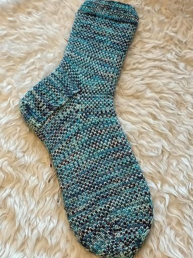 Nahaufnahme einer gestrickten Socke in Türkis und Blau mit sichtbarer Ferse