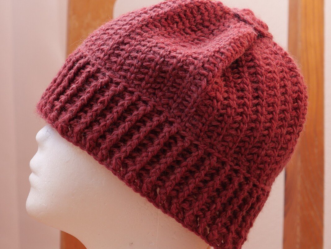 Bordeauxrote gehäkelte Mütze mit Rippenbund auf weißem Schaufensterkopf