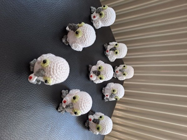 Mehrere weiße gehäkelte Amigurumi-Eulen mit grünen Augen und grauen Flügeln auf dunklem Untergrund
