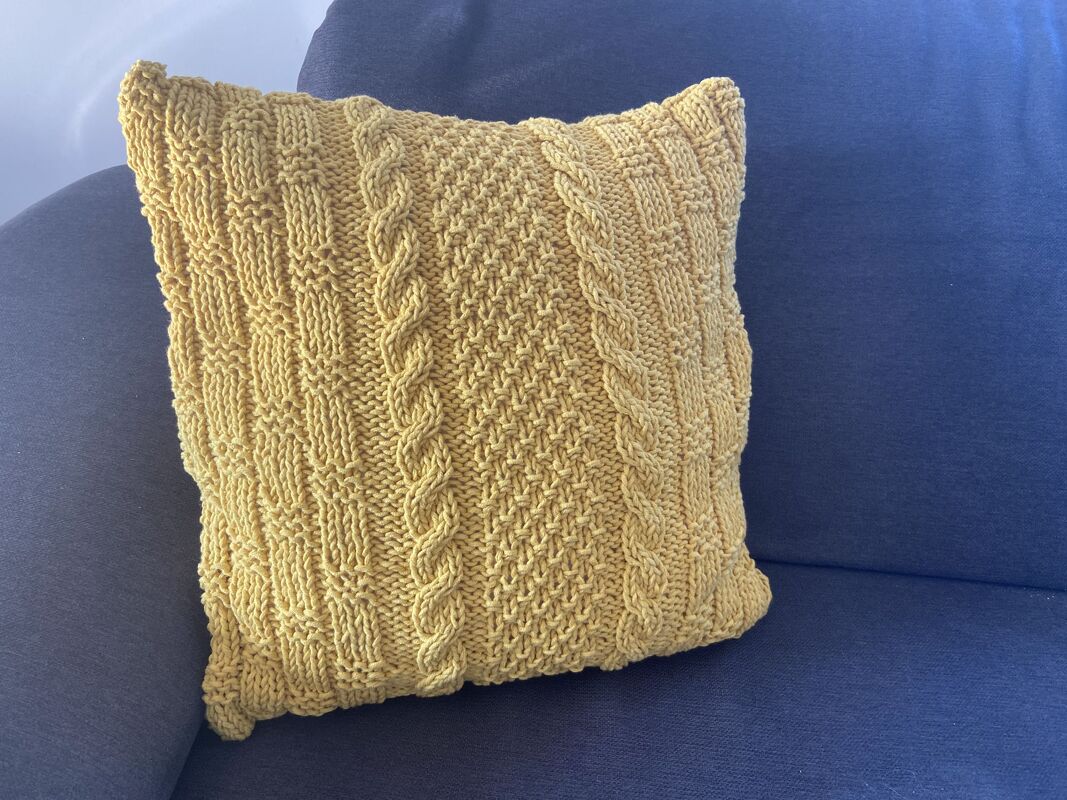 Senfgelbes gestricktes Kissen mit Zopfmuster auf blauem Sofa