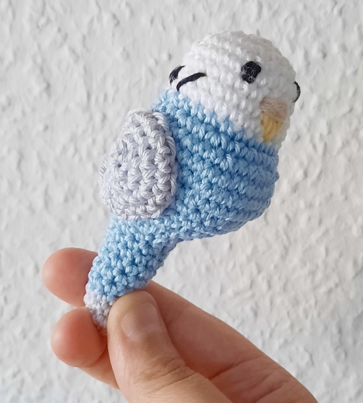 Hand hält gehäkelten blauen und weißen Wellensittich-Amigurumi
