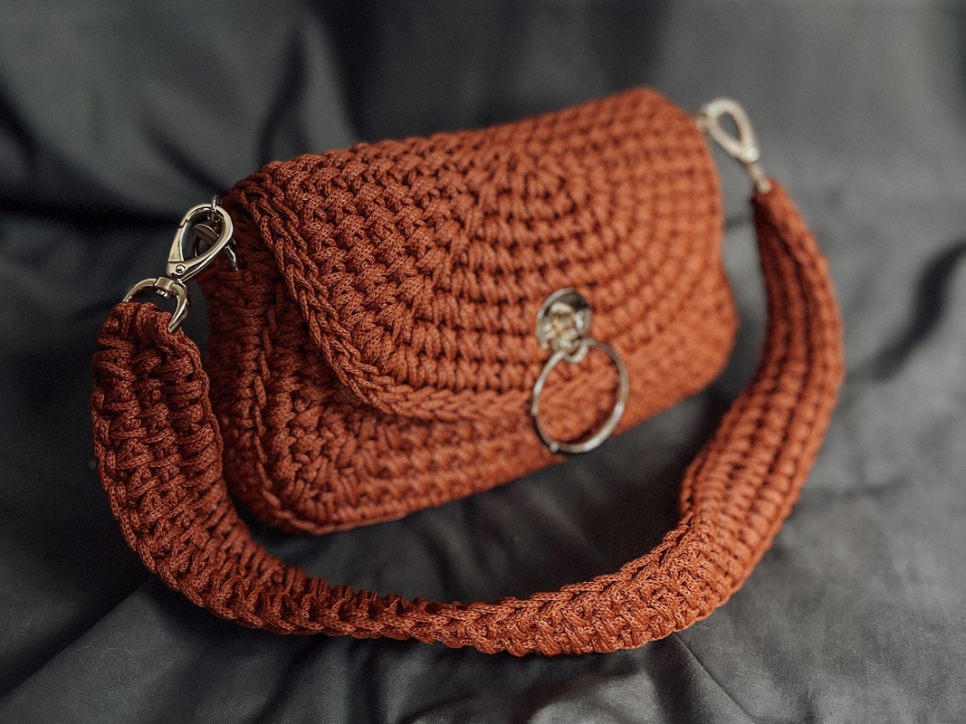 Rust crochet handle bag with flap, metal ring closure and detachable wide strap on dark background