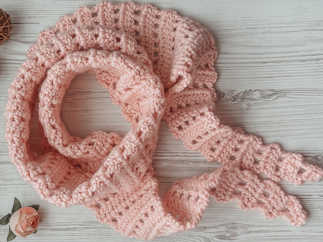 Detailed close-up of a soft pink crochet dragon-tail scarf showing scalloped tail points and open stitch rows