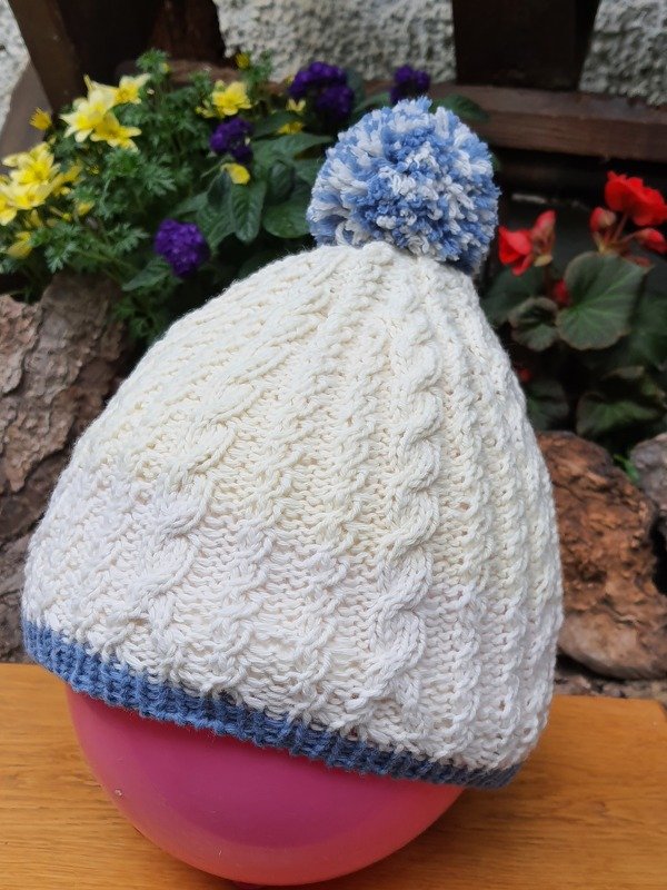 Gestrickte cremeweiße Zopfmütze mit hellblauer Kante und Bommel