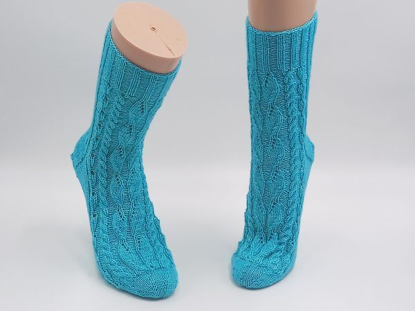 Zwei türkisfarbene, gestrickte Damensocken mit Zopf- und Ajourmuster auf Mannequin-Beinen vor weißem Hintergrund.