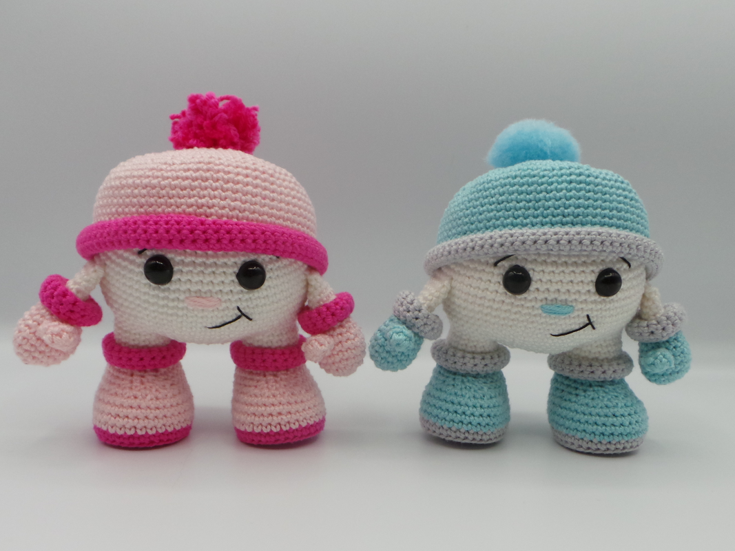 Zwei Amigurumi-Püppchen in Rosa und Hellblau mit Bommelmützen