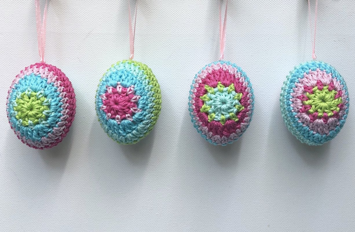 Four pastel crocheted Easter egg ornaments with star motifs and pink ribbons on a white background.
