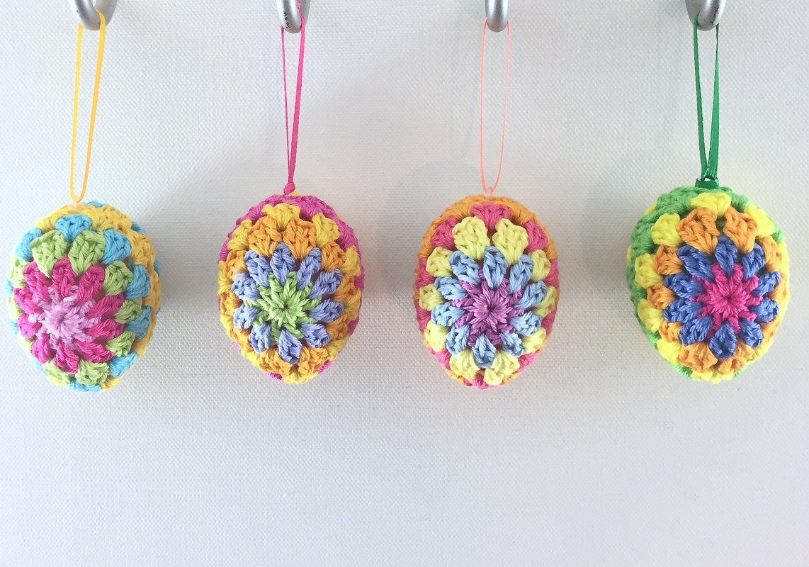 Four pastel crochet Easter egg ornaments with colored ribbon hangers on hooks