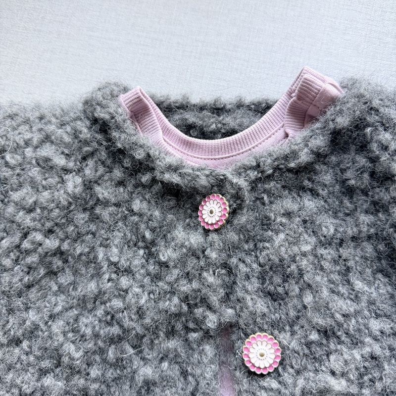 Kuschelige graue Kinderjacke aus Bouclé mit rosa Blumenknöpfen über rosa Oberteil