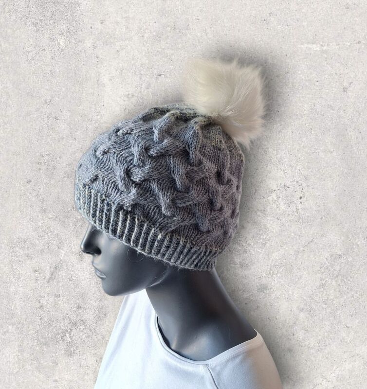 graue Strickmütze mit Rippbund, Zopfmuster und hellem Bommel auf Schaufensterkopf
