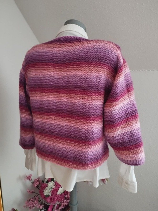 Rückenansicht einer kurz geschnittenen gestrickten Damenjacke mit horizontalen Streifen in Rosa- und Lilatönen auf einer Schneiderpuppe.