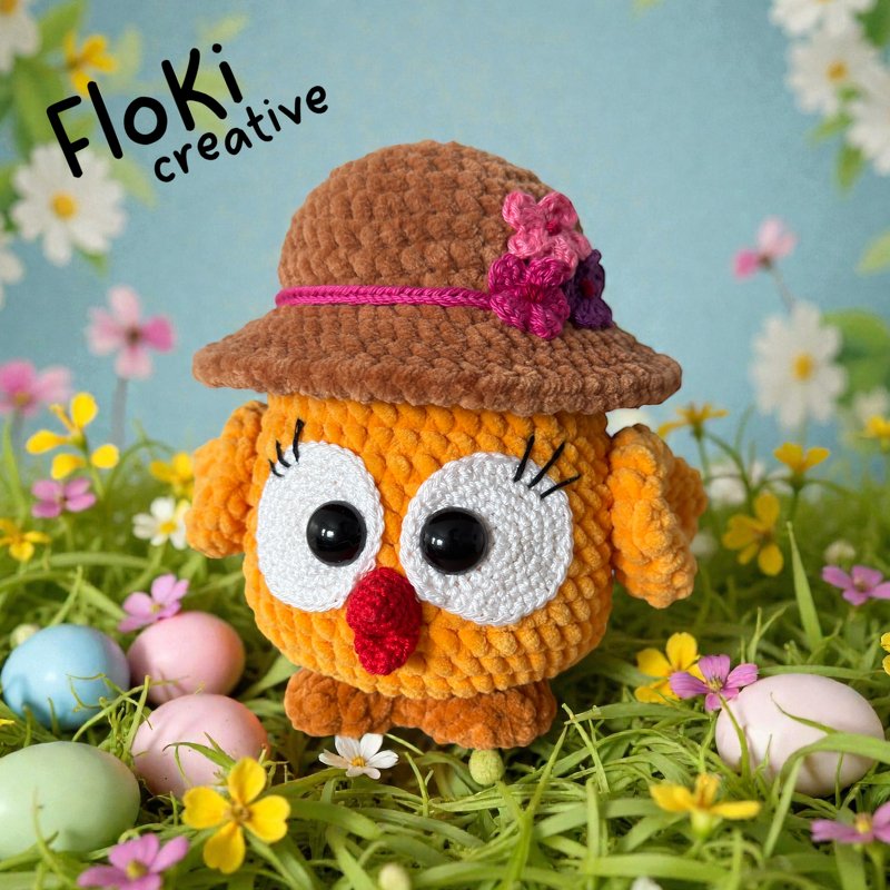 Gehäkelte orange Eule mit braunem Hut und bunten Ostereiern im Gras