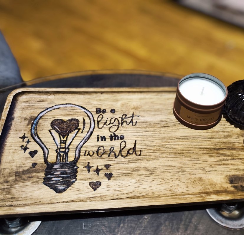 Hell geöltes Holztablett mit graviertem Motiv: Glühbirne mit Herz und dem Schriftzug „Be a light in the world“.