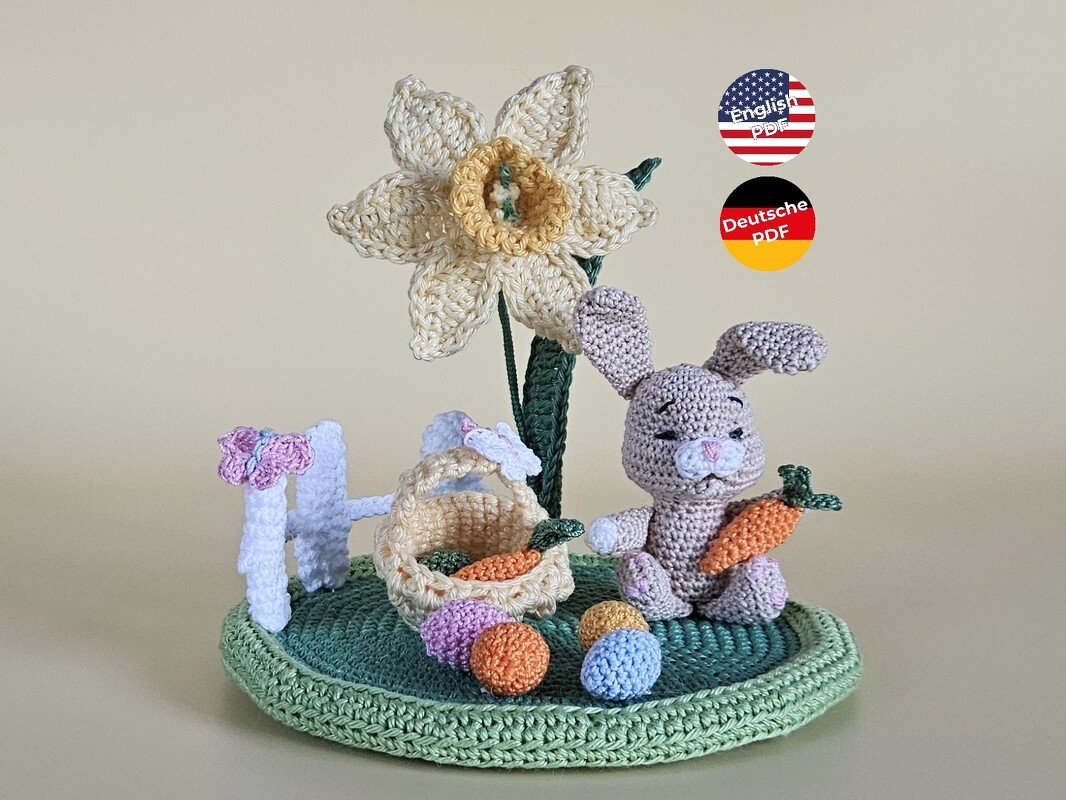 Gehäkelter Amigurumi-Hase mit Karotte, Narzisse und Korb mit bunten Ostereiern auf rundem Häkeluntergrund