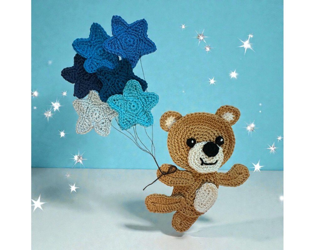 Whimsical crocheted bear holding several blue, dark blue, and light grey star-shaped crochet motifs on strings