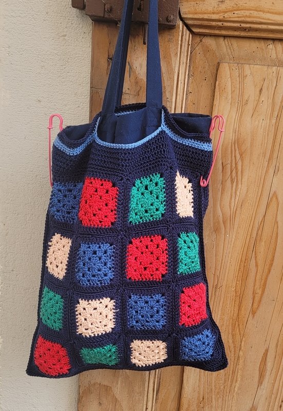 Dunkelblaue Henkeltasche mit bunten Granny Squares an einer Holztür