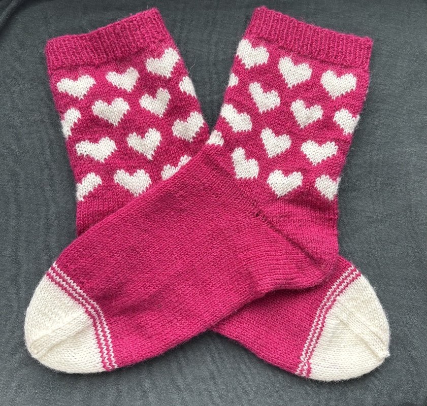 Handgestrickte pinke Socken mit weißen Herzen, gekreuzt auf dunklem Stoff