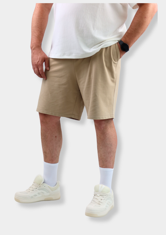 Beigefarbene Shorts mit Hand in Tasche, weißes T‑Shirt und helle Schuhe.