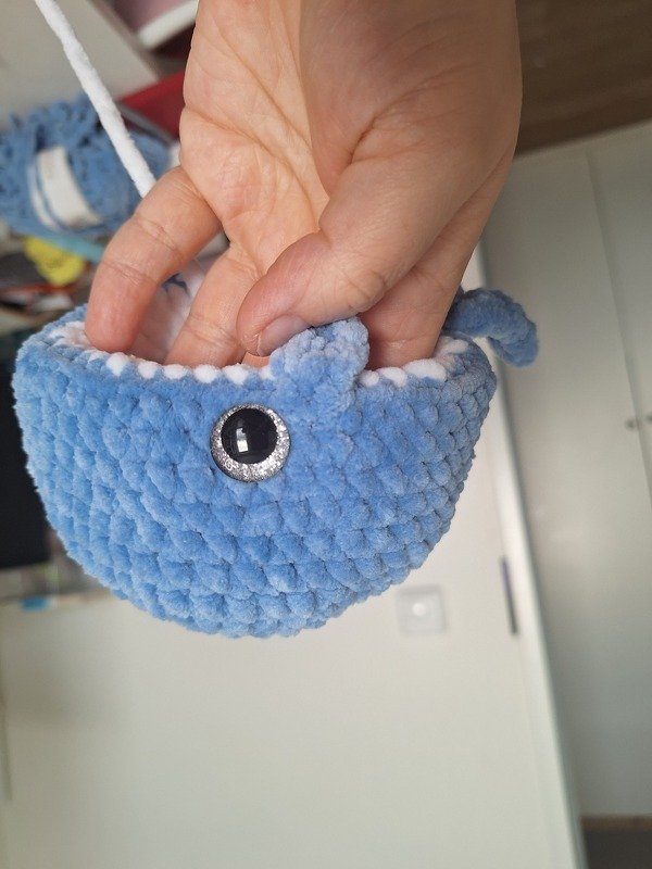 Hand hält kleinen blauen gehäkelten Wal-Amigurumi mit dekorativem Knopfauge und weißer Kante.
