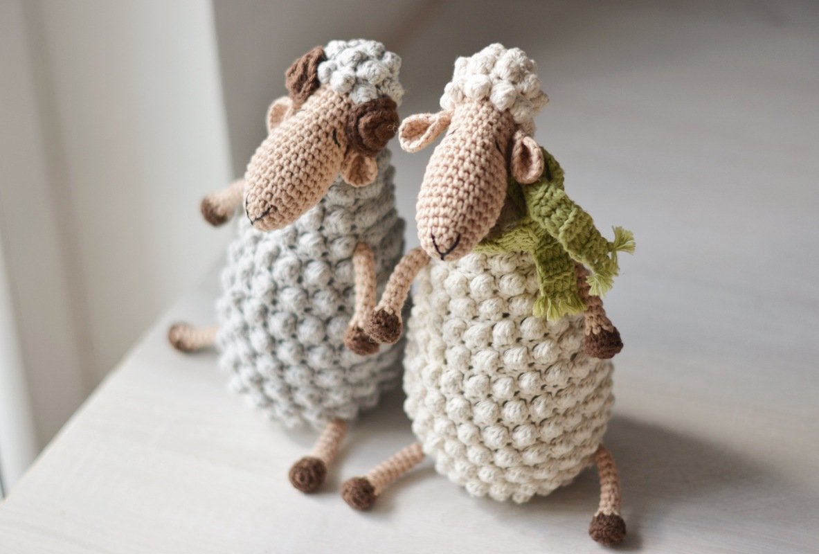 Zwei gehäkelte Amigurumi-Schafe in Grau und Creme mit Noppenstich-Körper und grünem Schal auf hellem Untergrund