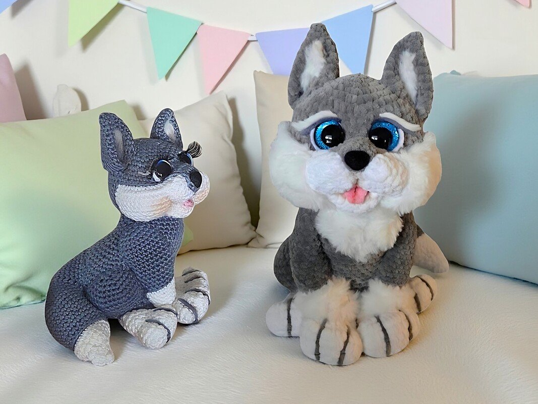 Two grey and white amigurumi wolf puppy toys with textured stitches sitting on a light sofa with pastel bunting