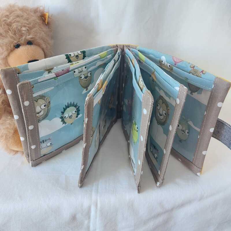 Offenes Stoffbuch mit Tiermotiven auf hellblauem Himmel und braun-gepunkteten Rändern