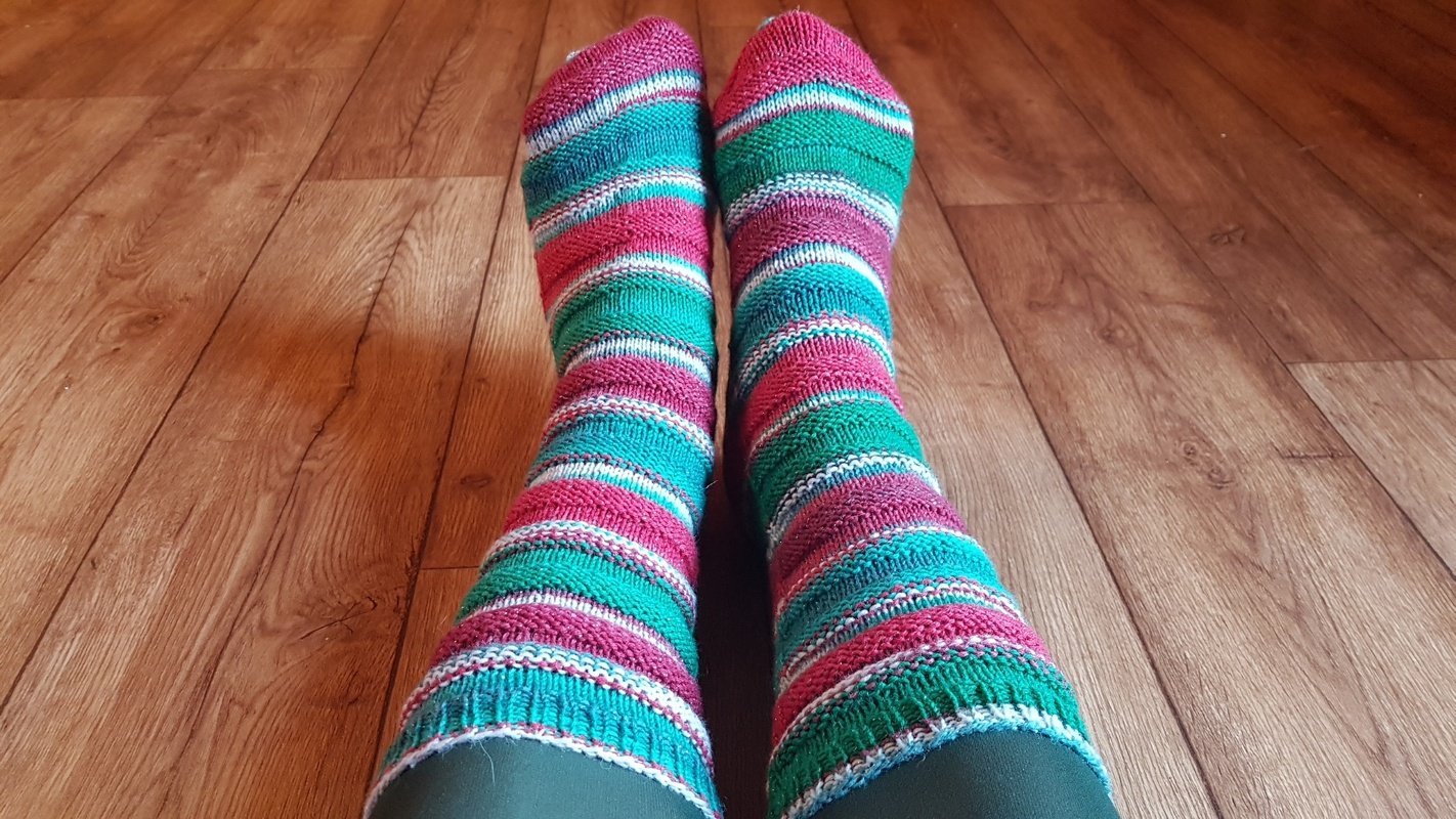 Bunte gestrickte Ringelsocken in Türkis, Grün und Rosa auf Holzfußboden