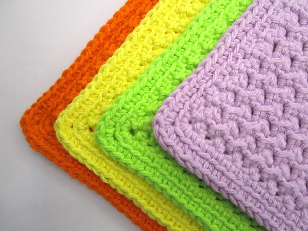 Vier übereinandergelegte gehäkelte Topflappen in Orange, Gelb, Neongrün und Lila, Nahaufnahme der Maschenstruktur