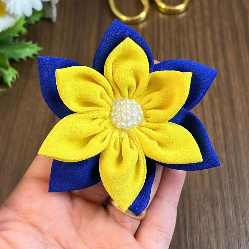 Hand holding a layered yellow and blue fabric flower with a pearl bead center