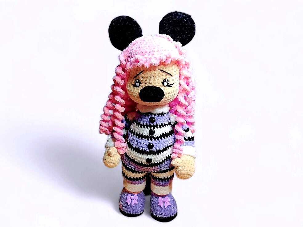 Gehäkelte Amigurumi-Puppe mit rosa Locken, runden schwarzen Ohren und gestreiftem Overall.