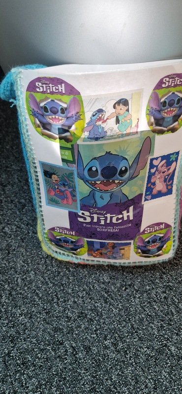 Gehäkelte Tasche weiß mit blau-grünem Rand, dekoriert mit mehreren Bildern eines blauen Cartoon-Charakters.