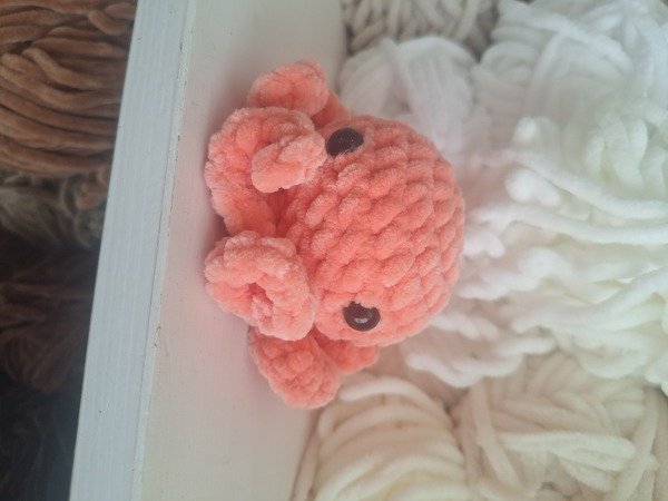 kleiner gehäkelter Oktopus aus korallfarbenem samtgarn mit dunklen Augen