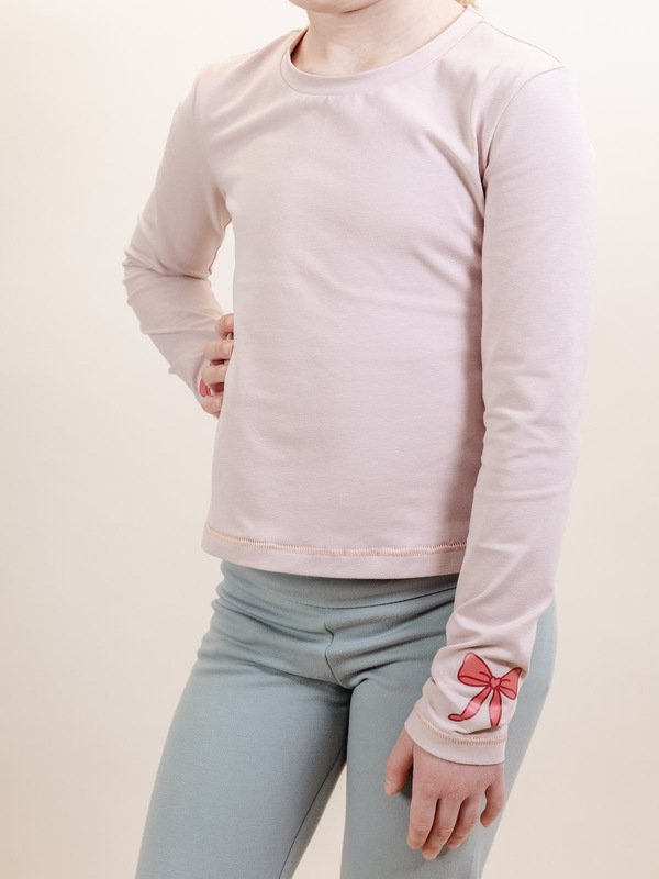 Child wearing crew-neck long-sleeve tee with printed bow on cuff and slim leggings
