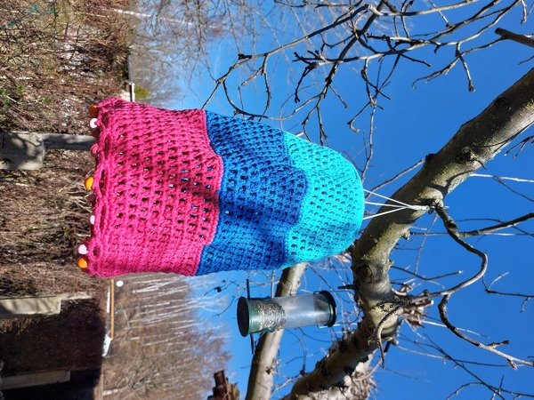 Gehäkelte dreifarbige Lampionhülle in Pink, Blau und Türkis an einem Baumzweig
