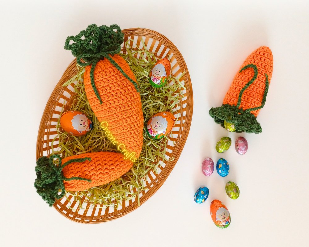 Crocheted carrot pouch with small foil-wrapped eggs beside it, next to a basket with more crocheted carrots and green paper grass.