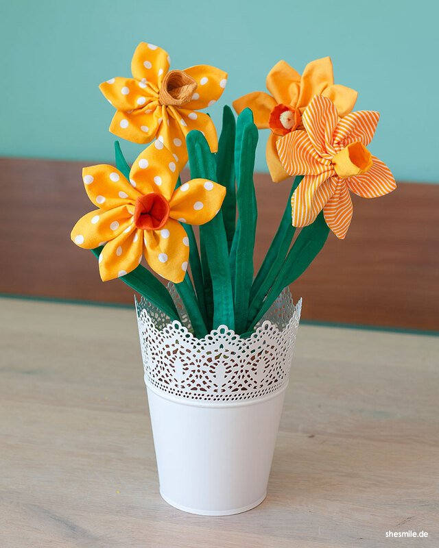 Genähte gelbe und orangefarbene Osterglocken aus Stoff mit grünen Blättern in einem weißen Topf